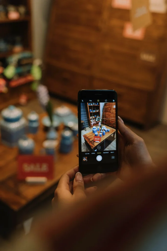 A person holding a smartphone capturing a photo of a display of items in a store, possibly for digital marketing or online promotion.